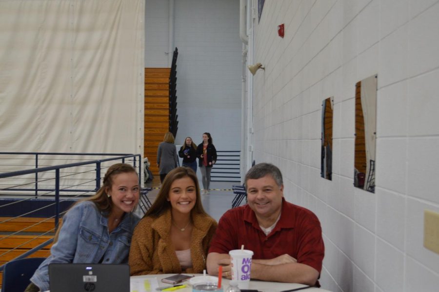 Seniors Kaci Geodde and Ella Lewis sit at the sign in table with Duel Credit History teacher and blood drive sponsor James Sisk.