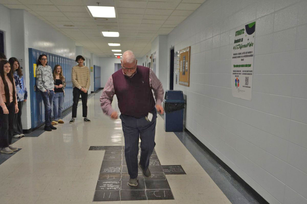 Accounting teacher Eric Brandenburg shows off how to play hopscotch he drew in the 200s hallway. "There was just this big black hole and something needed to be there," said Brandenburg.