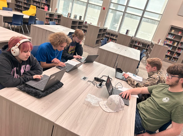 Clockwise from left, sophomores Madisynn Edwards, Cedric Green, Hayden Middleton, Owen Duggins, and Anthony Martin work on a Civics project in the library on March 12. The project in Jedy Hodge's class involves making a product to sell. The group chose friendship bracelets for their product.