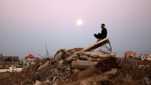 A man sits on top of a pile of rubble in the al-Bureij refugee camp in the central Gaza Strip, © 2024 Eyad Baba/AFP via Getty Images